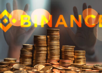 monedas apiladas sobre mesa con logo de binance en vidrio y persona detrás