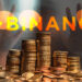 monedas apiladas sobre mesa con logo de binance en vidrio y persona detrás