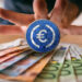 moneda de EURC sobre billetes de euto con mano detrás