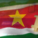 logo de bitcoin sobre bandera de Surinam con interfaz de la página web de BitcoinSranan en el fondo
