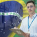 hombre sosteniendo tablilla con encuesta y bandera de Brasil al fondo