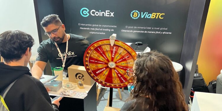 Tras personas conversando en el stand de CoinEx en la Blockchain Summit Latan 2024.