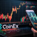 Una mano masculina sosteniendo un teléfono celular frente a una pantalla de computadora y el logo de CoinEx al lado.