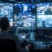 A focused security officer is overseeing a high-tech surveillance system with various live video feeds during a nighttime shift.