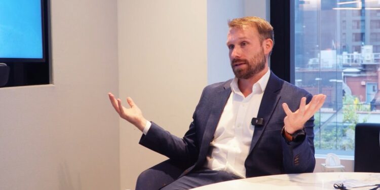 James Seyffart sentado en una sala de reuniones moderna con ventanal al fondo.
