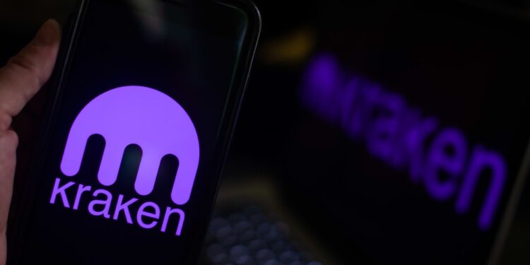 Una mano sostiene un smartphone en primer plano que muestra el logotipo de Kraken.