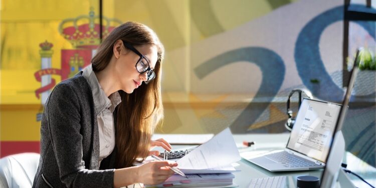 Mujer joven de lentes revisa documentos en el escritorio.