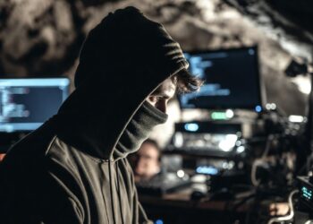 Un hombre con capucha y la cara cubierta frente a una computadora