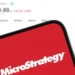 Un móvil con el logo de Microstrategy y en el fondo el precio de bitcoin.