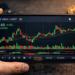 Gráfico de velas de USDC/USDT (tether y circle) en un smartphone sostenido por una mano, con indicadores de trading visibles
