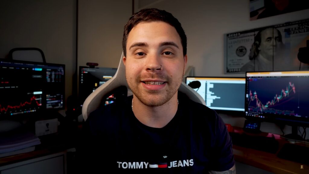 Fotografía de Agustín Nátoli sentado viendo a la camara con un fondo de pantallas mostrando graficos de velas.