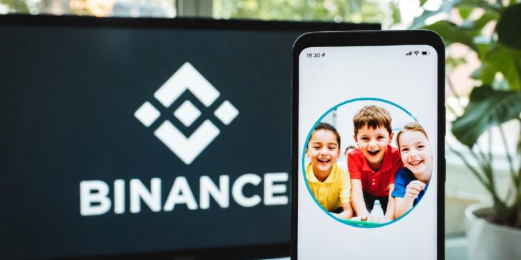 Logo de Binance en un monitor junto a un smartphone que tiene como fondo de pantalla a unos niños.