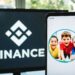 Logo de Binance en un monitor junto a un smartphone que tiene como fondo de pantalla a unos niños.