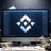 Logo de Binance en un monitor, rodeado de billetes y llaves.