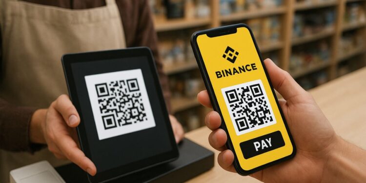 Una persona se encuentra en una tienda realizando un pago con su teléfono móvil. En la pantalla del celular se ve claramente el logotipo amarillo de Binance y un código QR con el botón “PAY” debajo. Frente a ella, un empleado sostiene una tableta negra que muestra otro código QR para recibir el pago. Ambos están en un mostrador de madera, con estantes llenos de productos desenfocados al fondo. La iluminación es cálida y natural, dando un ambiente acogedor y cotidiano, típico de una tienda moderna.