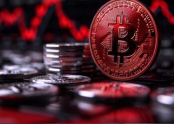 Moneda física de bitcoin con otras monedas alrededor y gráficas rojas.