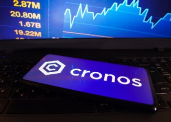 Teléfono móvil con el logo de cronos delante de un gráfico de precio.