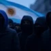 Encapuchados frente a una bandera de Argentina.