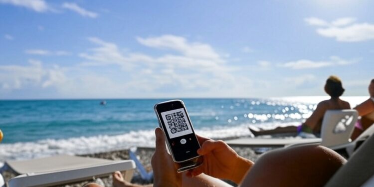 Una persona frente al mar a punto de hacer un pago por QR a través de su celular.
