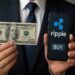 Empresario sostiene un billete de 100 dólares mientras muestra un teléfono móvil con el logo de Ripple y un botón de “comprar”.