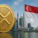 Una moneda dorada de XRP, detrás se aprecian rascacielos junto a la bandera roja y blanca de Singapur.