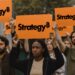 Personas protestando con carteles que muestran el logo de Strategy.