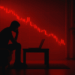Silueta de un hombre sentado frente a un portátil en una habitación oscura, con un gráfico rojo en la pared.