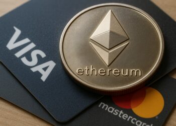 Moneda física de Ethereum plateada sobre dos tarjetas, una de Visa y otra de Mastercard.