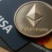 Moneda física de Ethereum plateada sobre dos tarjetas, una de Visa y otra de Mastercard.