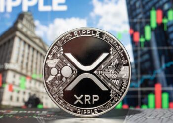 Moneda física de XRP en primer plano e imágenes típicas de Wall Street en el fondo.