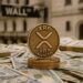 Moneda física de XRP dorada sobre billetes de dólares y el letrero de Wall Street.
